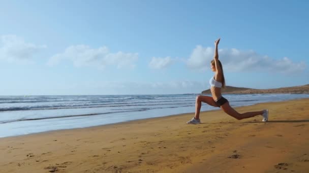 Женщина делает растяжки для ног. Фитнес-девушка, растягивающая ноги на пляжной тренировке. SLOW MIIION STEADICAM — стоковое видео