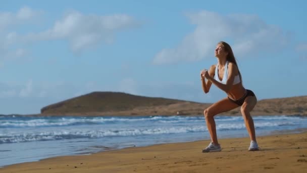 Sportswoman Porter des vêtements de sport Faire de l'exercice squats à l'extérieur. Fitness Femme Entraînement sur la plage au coucher du soleil. Athlétique jeune femme est engagée dans des sports de plein air . — Video