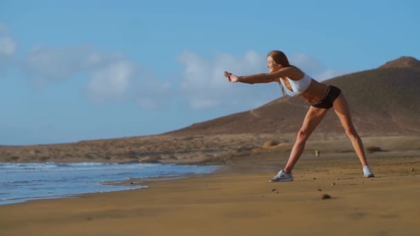 妇女伸展腿部和腿筋做站立前弯曲瑜伽伸展姿势在海滩上。健身妇女放松和练习运动和瑜伽上. — 图库视频影像