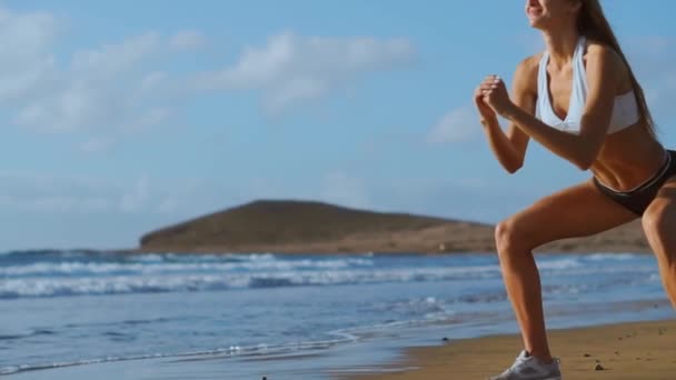 Молодая женщина, занимающаяся керлингом и упражнениями на приседание на пляже. спортивная девушка, приседающая на ногах, как часть активной и здоровой жизни. stedicam shoot — стоковое видео