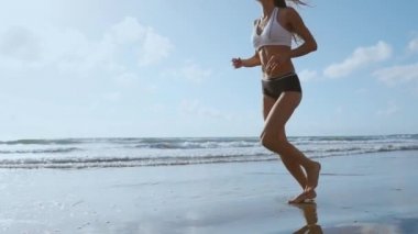 Plajda koşan fitness koşucusu kadın telefon kılıfı kolluk bandıyla müzik dinliyor. Spor atleti yaz güneşi altında çıplak ayakla kardiyo antrenmanı yapıyor..