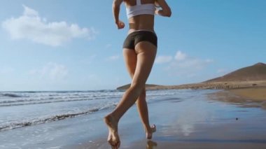 Plajda koşan fitness koşucusu kadın telefon kılıfı kolluk bandıyla müzik dinliyor. Spor atleti yaz güneşi altında çıplak ayakla kardiyo antrenmanı yapıyor..