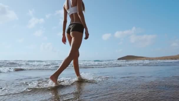 Γυναίκα ξυπόλητη περπατούσε στην καλοκαιρινή παραλία. κοντά πόδι της νεαρής γυναίκας με τα πόδια κατά μήκος του κύματος των θαλασσινών υδάτων και της άμμου στην παραλία. Έννοια ταξιδιού. — Αρχείο Βίντεο