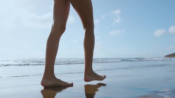 Een vrouw met blote voeten die over het zomerstrand loopt. close-up been van jonge vrouw wandelen langs de golf van zeewater en zand op het strand. Reisconcept. — Stockvideo