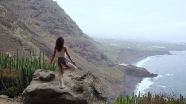 Genç kadın bir bacak kadar ellerini yükselterek üzerinde okyanus duran bakan bir adada dağlarda yoga yaparken