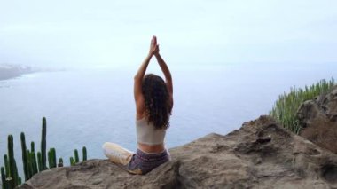 Genç kadının yoga meditasyon Lotus bulunduğu bir dağın tepesinde bir kayaya oturan okyanusa bakan bir adada dağlarda yapması