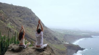 Bir adam ve bir kadın kadar ellerini yükselterek ve rahatlatıcı bir nefes gerçekleştirme meditasyon bir taş üzerinde oturan okyanus bakarak bir dağın tepesinde oturuyordu. Kanarya Adaları