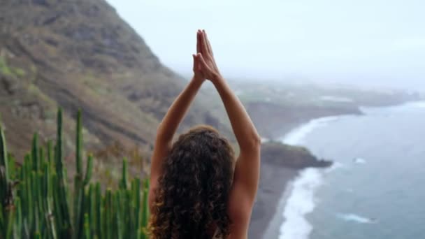 Mujer joven haciendo yoga en las montañas en una isla con vistas al océano sentada en una roca en la cima de una montaña meditando en posición de Loto — Vídeo de stock
