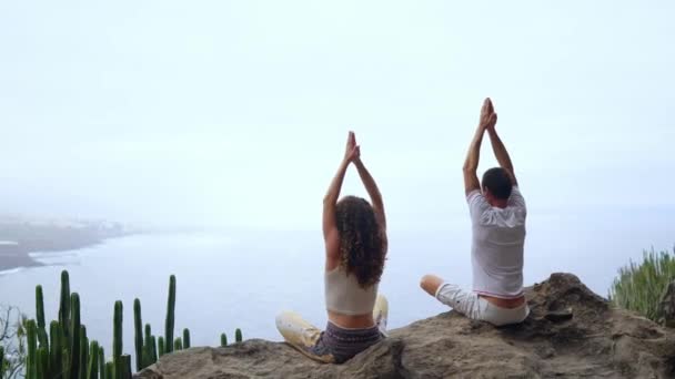 Bir adam ve bir kadın kadar ellerini yükselterek ve rahatlatıcı bir nefes gerçekleştirme meditasyon bir taş üzerinde oturan okyanus bakarak bir dağın tepesinde oturuyordu. Kanarya Adaları — Stok video