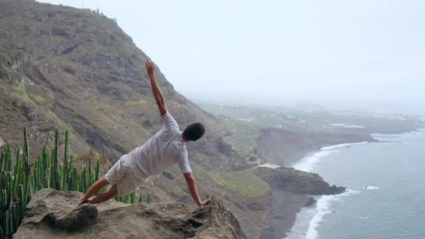 Een man die aan de ene kant in de bergen met zijn rug naar de camera kijken naar de Oceaan en mediteren op de Canarische eilanden. — Stockvideo