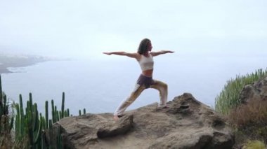 Kadın meditasyon yoga savaşçı poz, okyanus, plaj ve rock Dağları. Motivasyon ve ilham verici uyum ve egzersiz. Açık havada doğa, fitness kavramı içinde sağlıklı yaşam tarzı.