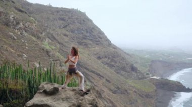 Kadın meditasyon yoga savaşçı poz, okyanus, plaj ve rock Dağları. Motivasyon ve ilham verici uyum ve egzersiz. Açık havada doğa, fitness kavramı içinde sağlıklı yaşam tarzı.