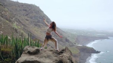 Kadın meditasyon yoga savaşçı poz, okyanus, plaj ve rock Dağları. Motivasyon ve ilham verici uyum ve egzersiz. Açık havada doğa, fitness kavramı içinde sağlıklı yaşam tarzı.