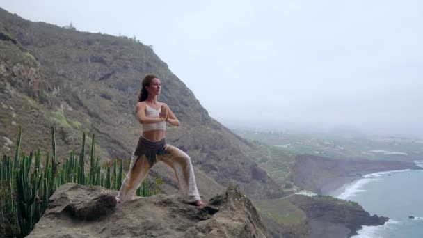 Gün batımında yoga bir kayalık sahil üzerinde yaparken genç kadın. Sağlıklı bir yaşam tarzı kavramı. Uyum. İnsan ve doğa. Arka plan mavi okyanusun. — Stok video