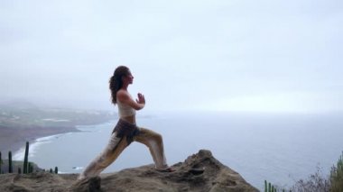 Gün batımında yoga bir kayalık sahil üzerinde yaparken genç kadın. Sağlıklı bir yaşam tarzı kavramı. Uyum. İnsan ve doğa. Arka plan mavi okyanusun.