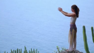 Gün batımında yoga bir kayalık sahil üzerinde yaparken genç kadın. Sağlıklı bir yaşam tarzı kavramı. Uyum. İnsan ve doğa. Arka plan mavi okyanusun.