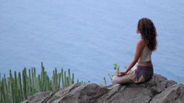 Genç kadının yoga meditasyon Lotus bulunduğu bir dağın tepesinde bir kayaya oturan okyanusa bakan bir adada dağlarda yapması
