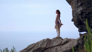 Gün batımında yoga bir kayalık sahil üzerinde yaparken genç kadın. Sağlıklı bir yaşam tarzı kavramı. Uyum. İnsan ve doğa. Arka plan mavi okyanusun.