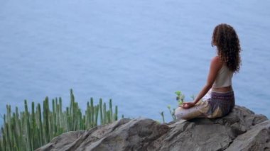 Genç kadının yoga meditasyon Lotus bulunduğu bir dağın tepesinde bir kayaya oturan okyanusa bakan bir adada dağlarda yapması.