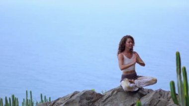 Genç kadının yoga meditasyon Lotus bulunduğu bir dağın tepesinde bir kayaya oturan okyanusa bakan bir adada dağlarda yapması