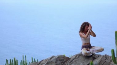 Genç kadının yoga meditasyon Lotus bulunduğu bir dağın tepesinde bir kayaya oturan okyanusa bakan bir adada dağlarda yapması
