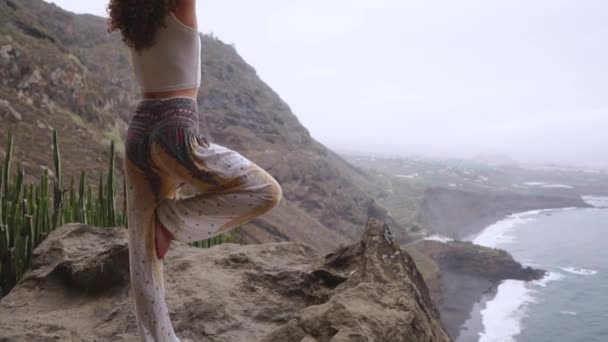 Mujer meditando en yoga guerrero posan en el océano, la playa y las montañas rocosas. Motivación y ajuste inspirador y ejercicio. Estilo de vida saludable al aire libre en la naturaleza, concepto de fitness . — Vídeo de stock