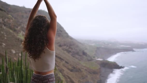 Женщина, медитирующая в йоге воина, позирует у океана, пляжа и скальных гор. Мотивация и вдохновляющее приспособление и упражнения. Здоровый образ жизни на природе, концепция фитнеса . — стоковое видео