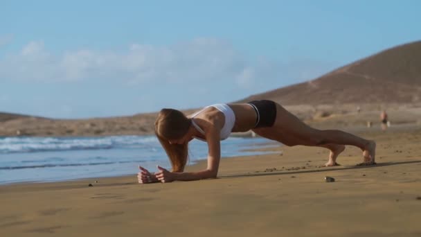 Вид збоку красивої спортивної жінки в дощатому положенні на пляжі під час заходу сонця . — стокове відео