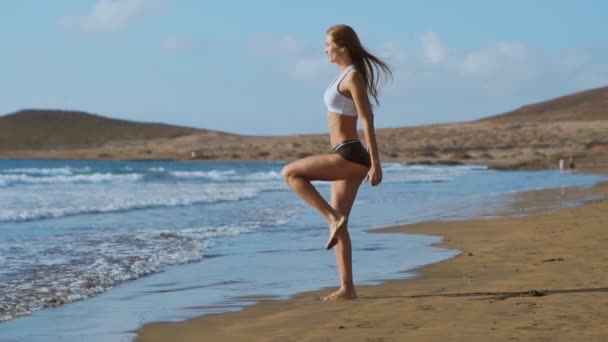 Ragazza sportiva su una spiaggia facendo esercizi affondi. Concetto di uno stile di vita sano — Video Stock