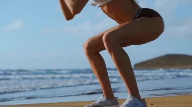 Çekirdek ve glutes plajda bodur egzersizleri yapıyor vücut ağırlığı egzersiz ile çalışan genç kadın fitness. sportif kız çömelme bacaklar aktif ve formda bir yaşamın bir parçası olarak. stedicam ateş
