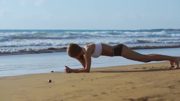 Zijaanzicht van mooie sportieve vrouw in plank positie op het strand tijdens zonsondergang. — Stockvideo