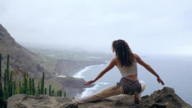 Okyanusa bakan bir poz savaşta bir uçurumun kenarında oturan bir kadın onun ellerini yukarı kaldır ve deniz havası yoga yaparken nefes