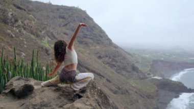 Okyanusa bakan bir poz savaşta bir uçurumun kenarında oturan bir kadın onun ellerini yukarı kaldır ve deniz havası yoga yaparken nefes