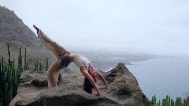 Kızı pratik yoga mavi gökyüzü ve masmavi denizin karşı buzlu. Kadın bir köprü duruş bir taş üzerinde duruyor.