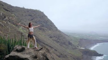 Gün batımında yoga bir kayalık sahil üzerinde yaparken genç kadın. Sağlıklı bir yaşam tarzı kavramı. Uyum. İnsan ve doğa. Arka plan mavi okyanusun.