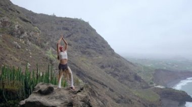 Gün batımında yoga bir kayalık sahil üzerinde yaparken genç kadın. Sağlıklı bir yaşam tarzı kavramı. Uyum. İnsan ve doğa. Arka plan mavi okyanusun.