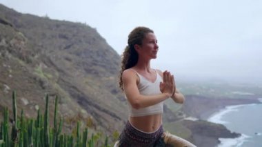 Gün batımında yoga bir kayalık sahil üzerinde yaparken genç kadın. Sağlıklı bir yaşam tarzı kavramı. Uyum. İnsan ve doğa. Arka plan mavi okyanusun.