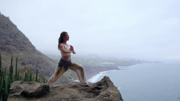 Mladá žena dělá jógu na skalnaté pobřeží při západu slunce. Koncept zdravého životního stylu. Harmonie. Člověk a příroda. Na pozadí modrý oceán. — Stock video