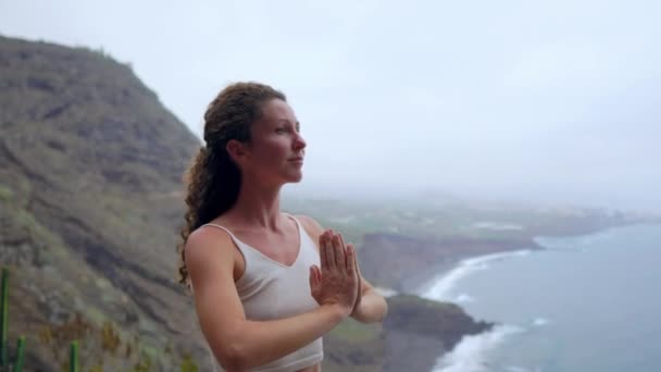 Mujer joven haciendo yoga en una costa rocosa al atardecer. El concepto de un estilo de vida saludable. Armonía. Humano y naturaleza. El fondo del océano azul . — Vídeo de stock