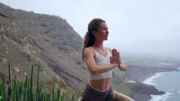 Jonge vrouw doet yoga op een rotsachtige kust bij zonsondergang. Het concept van een gezonde levensstijl. Harmonie. Mens en natuur. De achtergrond van de blauwe oceaan. — Stockvideo