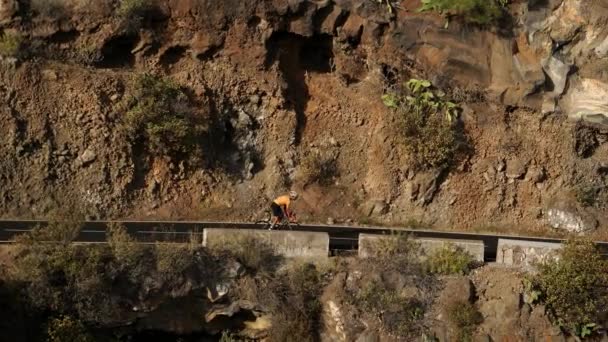 Un uomo in t-shirt gialla su una bici da strada sportiva cavalca sulla strada situata in alto in montagna — Video Stock