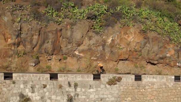 Un uomo in t-shirt gialla su una bici da strada sportiva cavalca sulla strada situata in alto in montagna — Video Stock