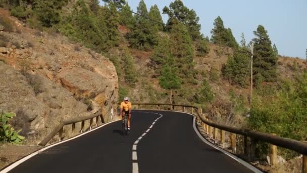 Un uomo in t-shirt gialla su una bici da strada sportiva cavalca sulla strada situata in alto in montagna — Video Stock