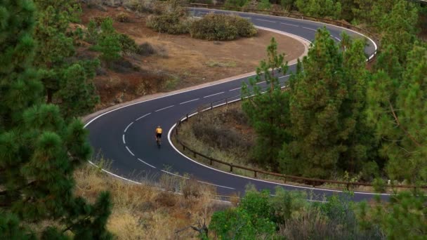 一个穿着黄色 t恤衫的人在公路上骑自行车在山上的高处行驶 — 图库视频影像