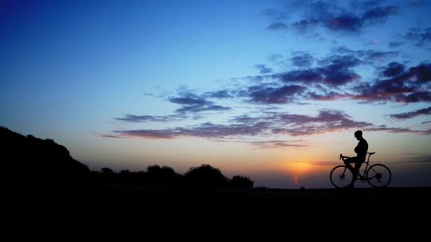 O homem está com uma bicicleta no fundo do pôr-do-sol. captura de lapso de tempo. Ângulo largo — Vídeo de Stock