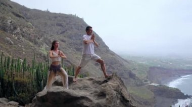Okyanusa bakan bir uçurumun kenarında duran bir kadın ve bir erkek kendi ellerini yukarı kaldır ve deniz havası yoga sırasında nefes