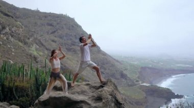 Okyanusa bakan bir uçurumun kenarında duran bir kadın ve bir erkek kendi ellerini yukarı kaldır ve deniz havası yoga sırasında nefes