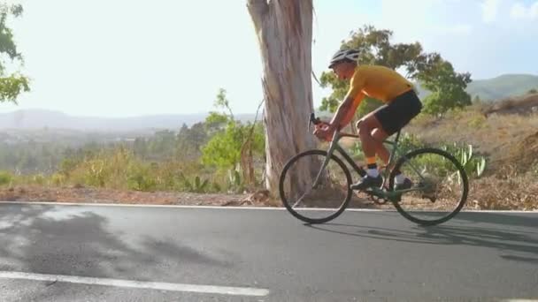 Bir adam yolda bisiklet binmek. Spor ve aktif bir yaşam konsepti günbatımı zamanı. Bir adam bir parkta bisiklet sürme. Bisikletçi vücut üzerinde turuncu güneş ışını ile mavi gökyüzü. — Stok video