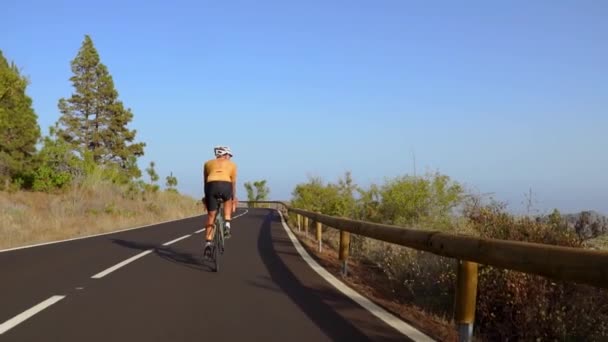 Un hombre en bicicleta en la carretera. Deporte y vida activa concepto puesta del sol tiempo. Un hombre montando en bicicleta en un parque. Cielo azul con rayo de sol naranja sobre el cuerpo del ciclista . — Vídeos de Stock