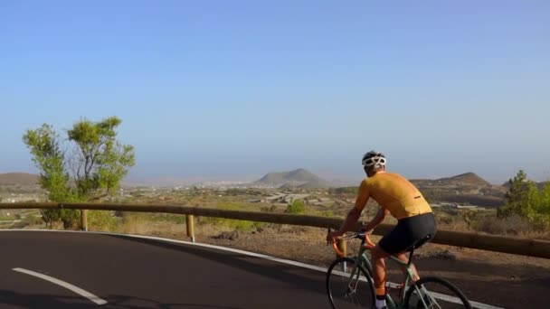 Tracking shot van de video van een mannelijke wielrenner klimmen op een bergweg. Man doet fietsen training op een heuvelachtig snelweg weg op een zonnige dag. — Stockvideo